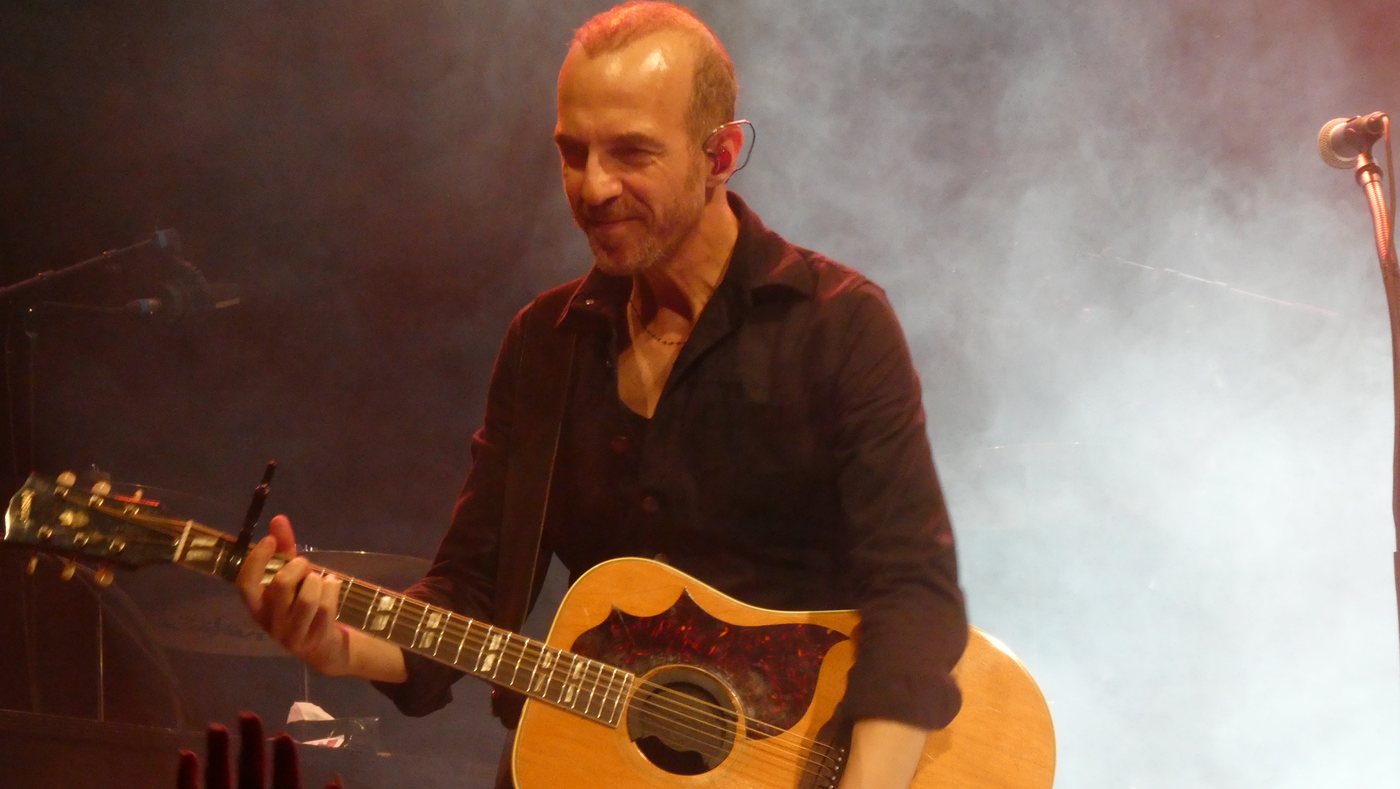 Calogero standing with an acoustic guitar on a theatre stage
