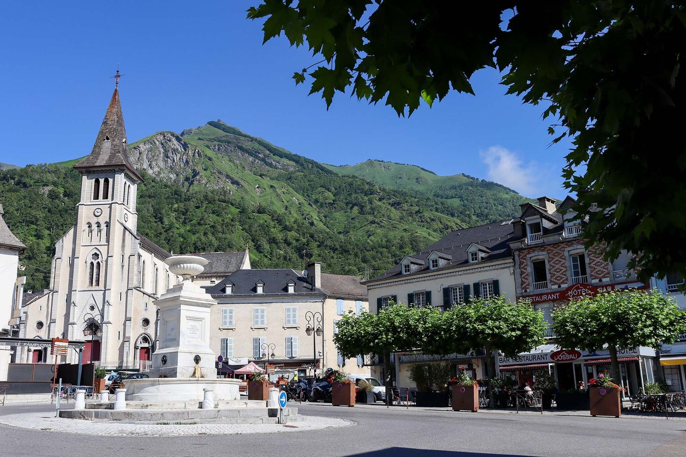 La place de Laruns, l'église et la fontaine, avec un sommet herbeux en arrière-plan